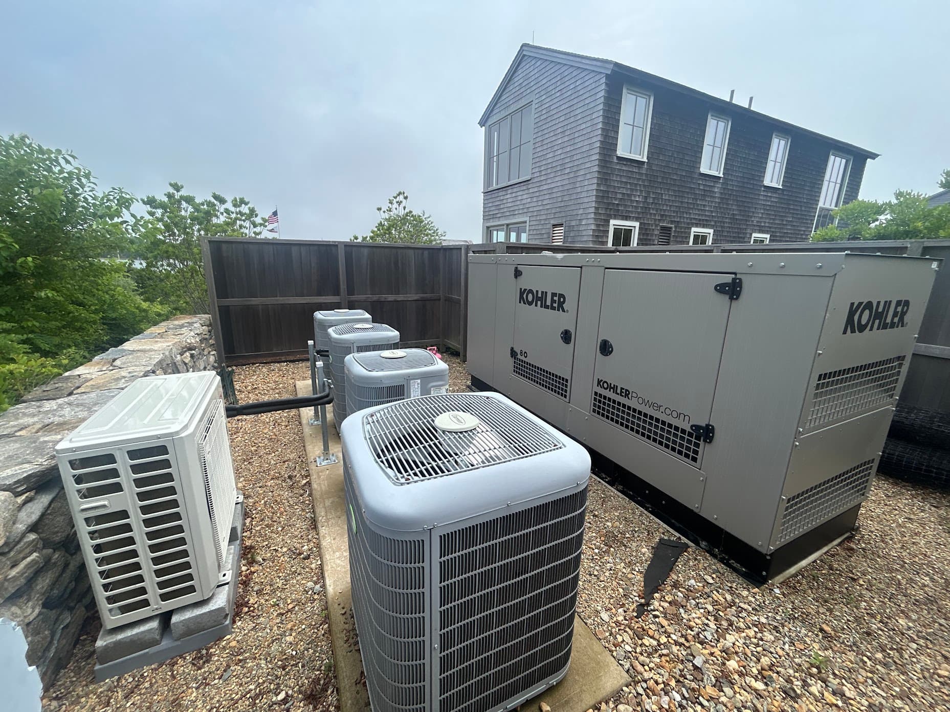 Four central air conditioning condensers installed on a coastal home, alongside a Kohler standby generator