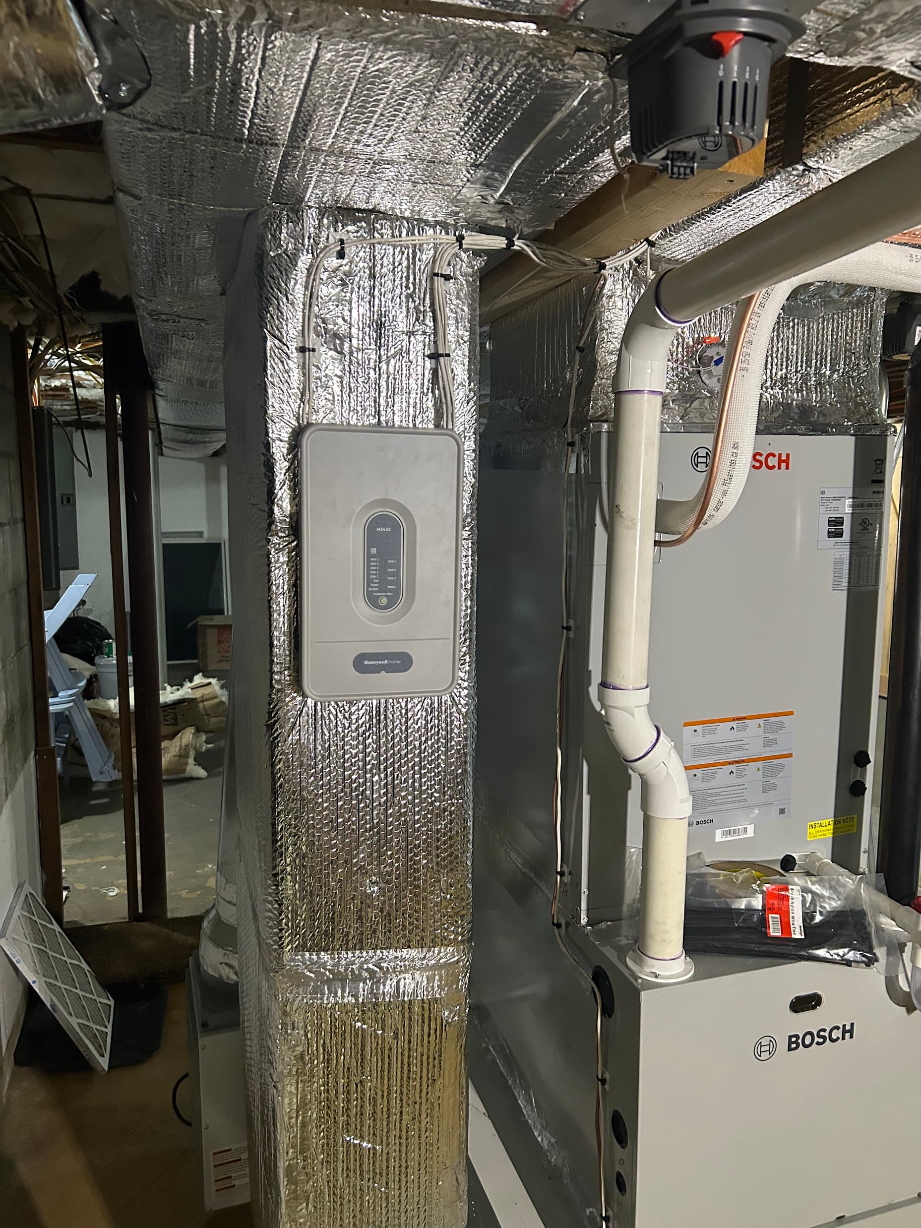 A Bosch heat pump air handler installed in a basement with a Honeywell zoning control panel