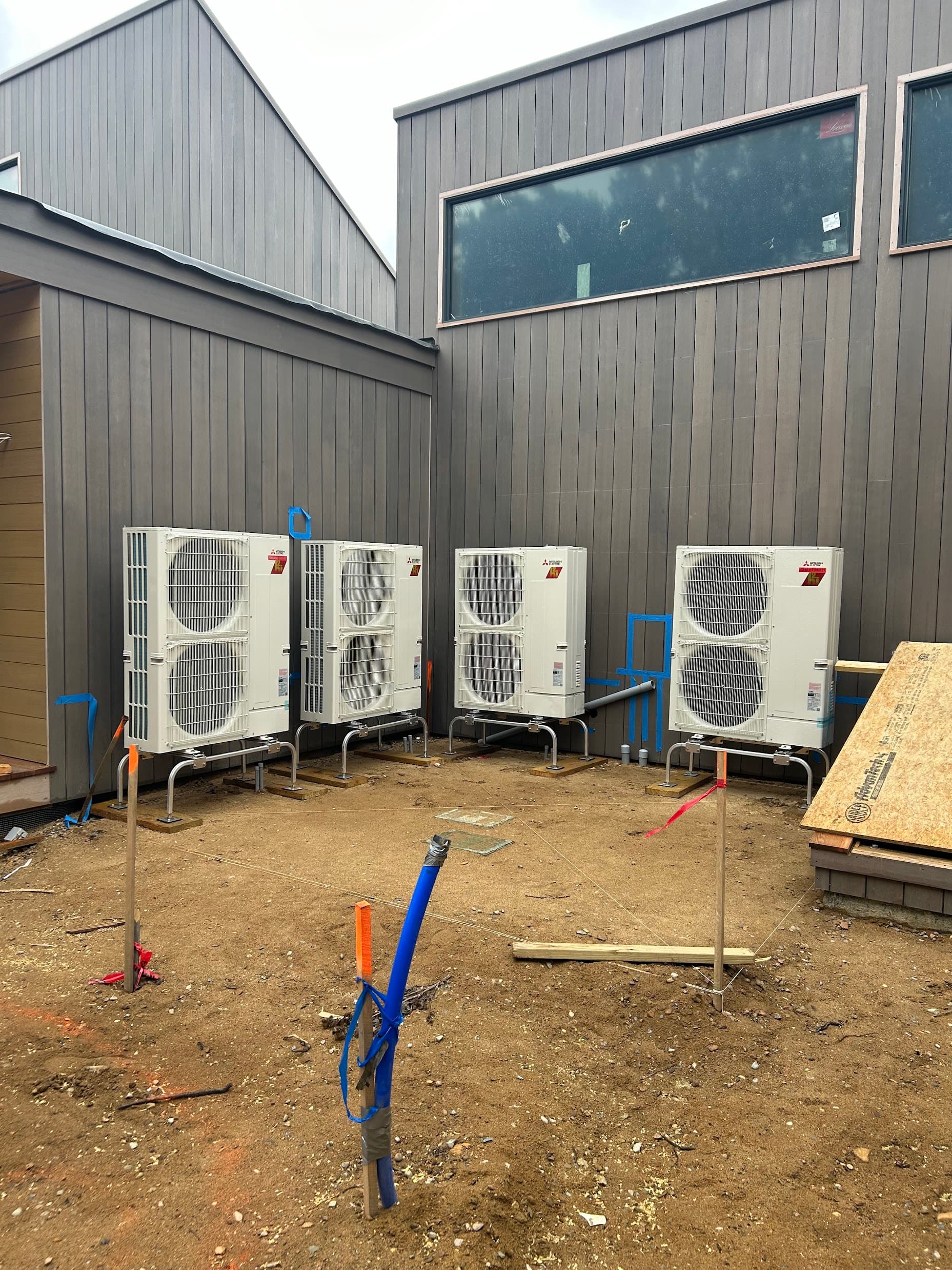 Four Mitsubishi ductless mini-split outdoor units installed on stands during new home construction